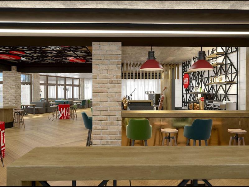 Área de lounge moderna de un hotel con mesas de madera, sillones coloridos y diseño industrial.