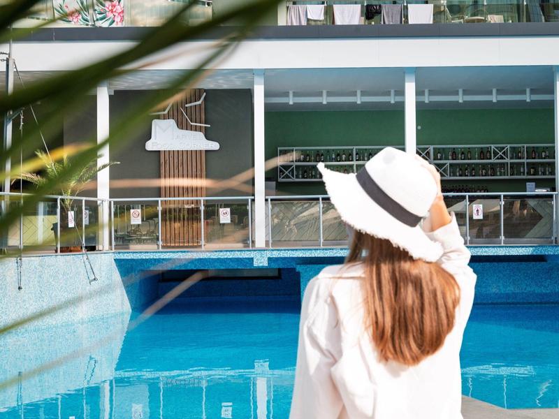 Mujer con sombrero blanco mira una piscina turquesa y un edificio moderno.