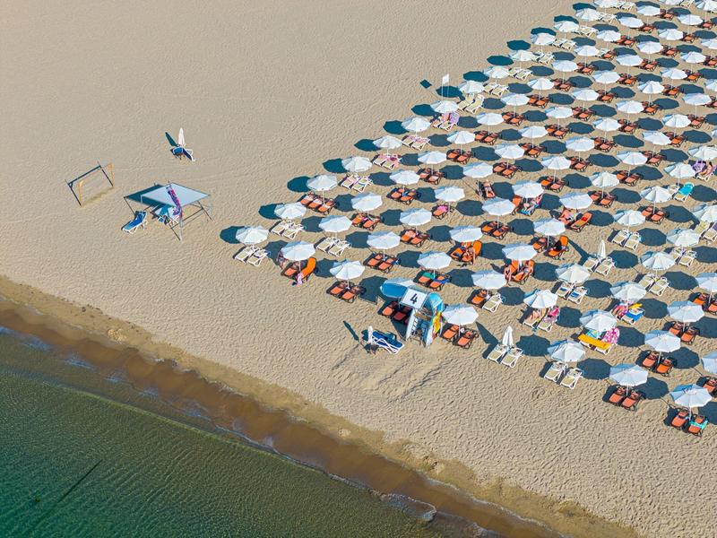 Vista aérea de una playa con filas de sombrillas y tumbonas junto al agua clara.