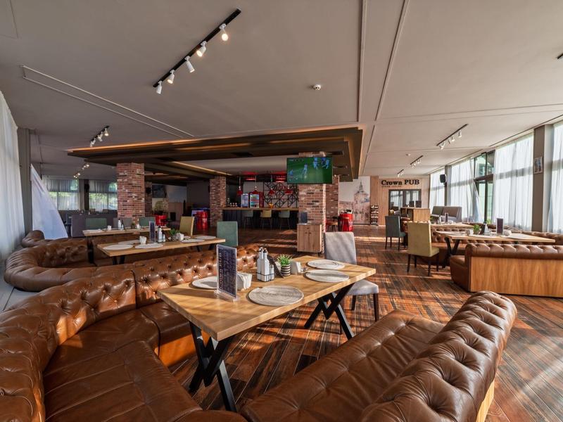 Restaurante de hotel luminoso con sofás de cuero marrón, mesas de madera y grandes ventanas con luz natural.