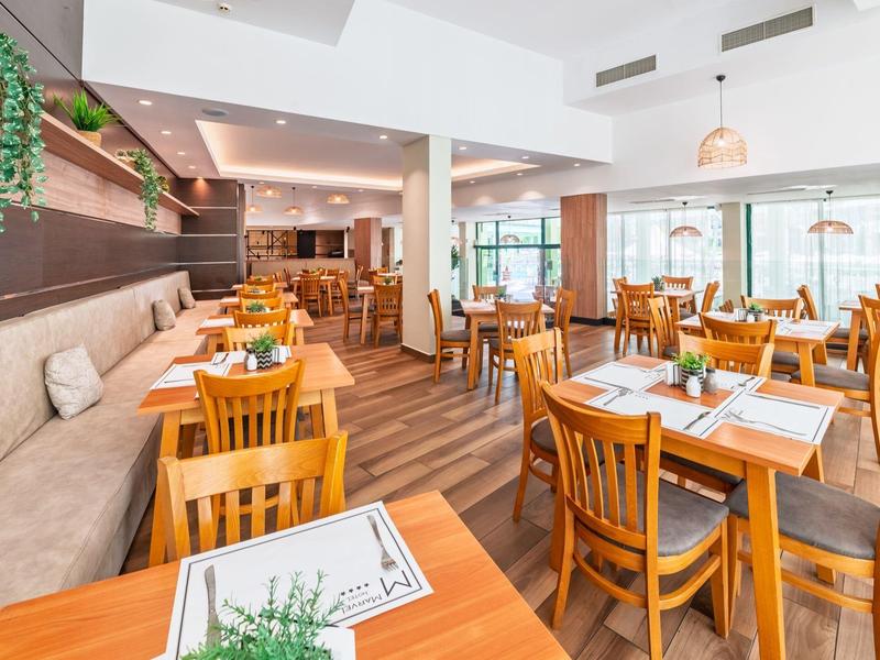Restaurante moderno con muebles de madera, grandes ventanas y mesas con plantas.