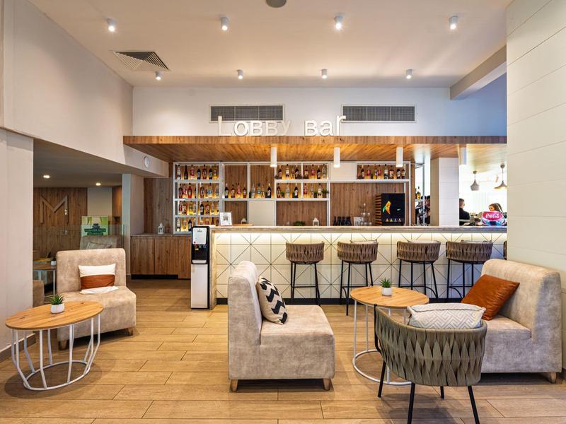 Moderna zona de lobby de hotel con barra, asientos cómodos y suelo de madera.