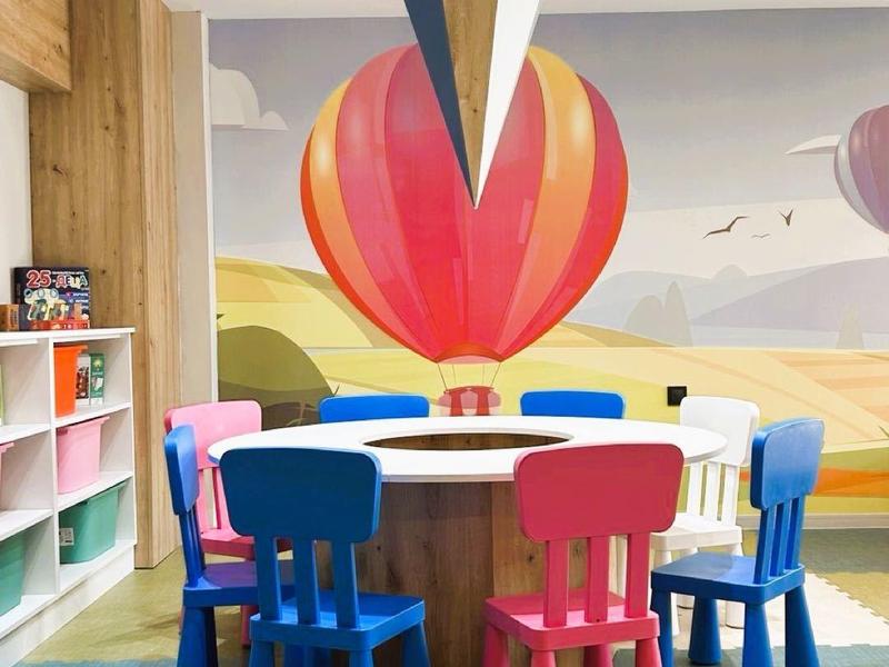 Colorida sala de juegos para niños con mesas redondas, sillas coloridas y decoración de pared de globo aerostático.