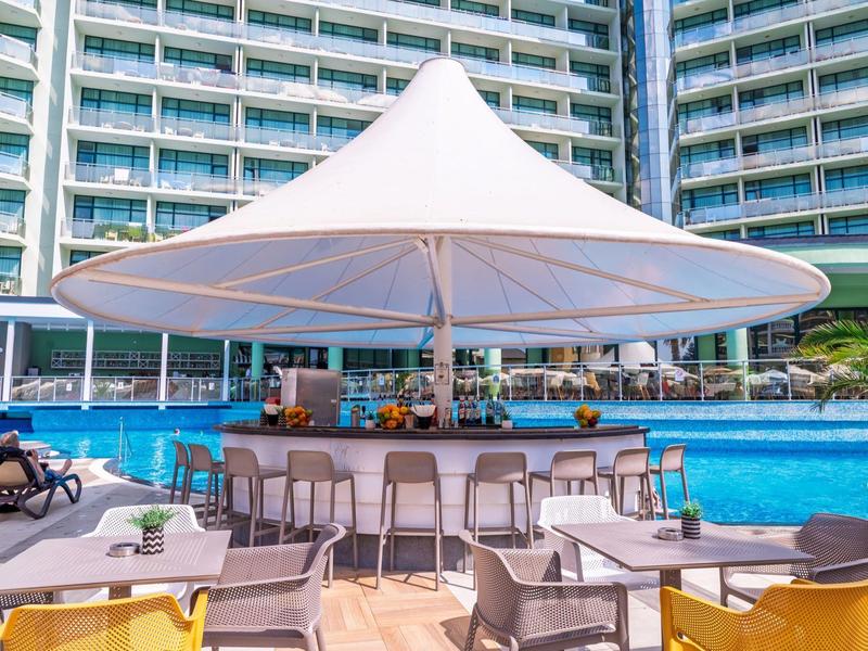 Piscina exterior moderna con bar y sombrilla frente a un edificio hotelero.