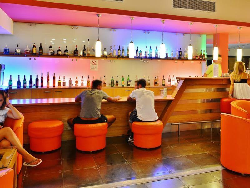 Bar moderna del hotel con muebles naranjas, huéspedes en la barra y luz de fondo de colores.