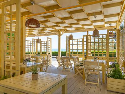 Světlá otevřená restaurace se dřevěným nábytkem a výhledem na zelenou přírodu.