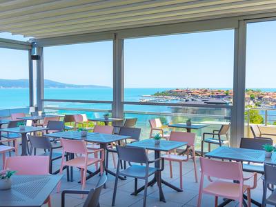 Moderní restaurace s barevnými židlemi a výhledem na moře přes velká okna.