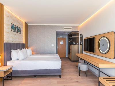 Moderní hotelový pokoj s manželskou postelí, dřevěnou podlahou a nepřímým osvětlením.