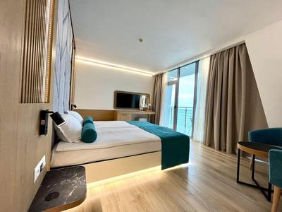 Modernes Hotelzimmer mit Doppelbett, TV, Balkon mit Meerblick und elegantem Holzboden.