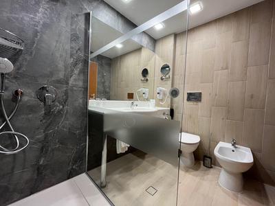 Modernes Badezimmer mit Glasdusche, Waschbecken, Toilette und Bidet in neutralen Farben.