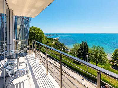 Balkon mit Stühlen und Tisch, Blick auf Meer und grünen Park bei sonnigem Wetter