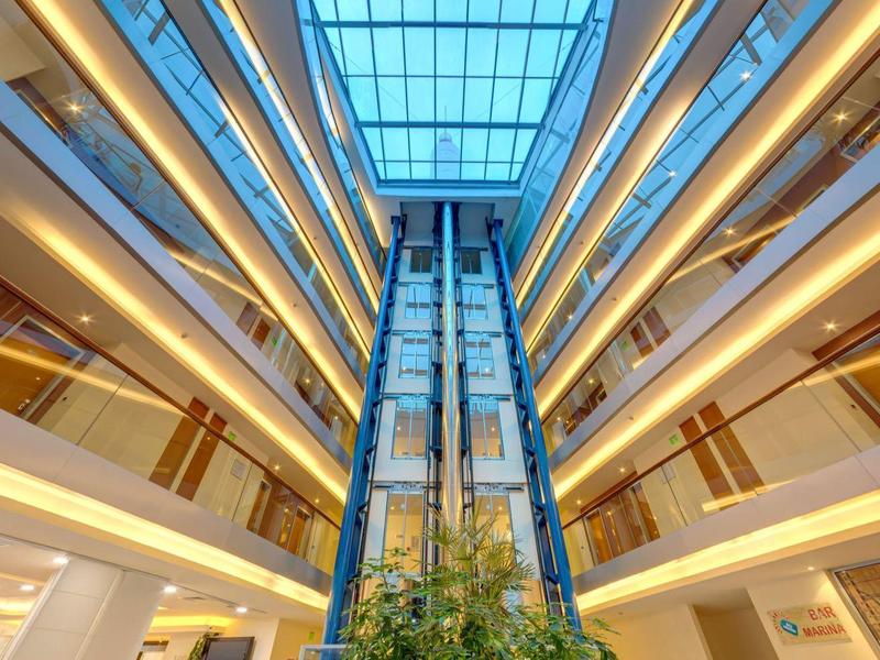 Modernes Einkaufszentrum mit Glasaufzug und mehreren Etagen unter einem großen Glasdach.