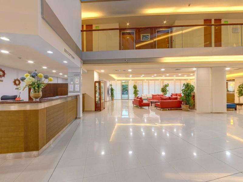 Große helle Hotelhalle mit Rezeption links, weißen Böden und roten Sesseln im Hintergrund.