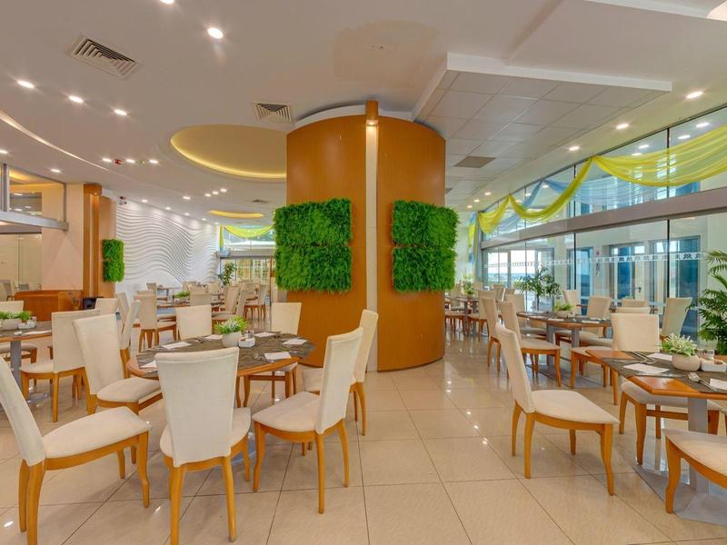 Helles, modernes Restaurant mit weißen Stühlen, runden Tischen und grünen Pflanzen an den Wänden.