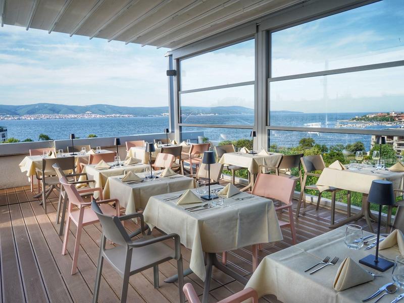 Dachterrassenrestaurant mit gedeckten Tischen und Blick auf den Hafen und das Meer.