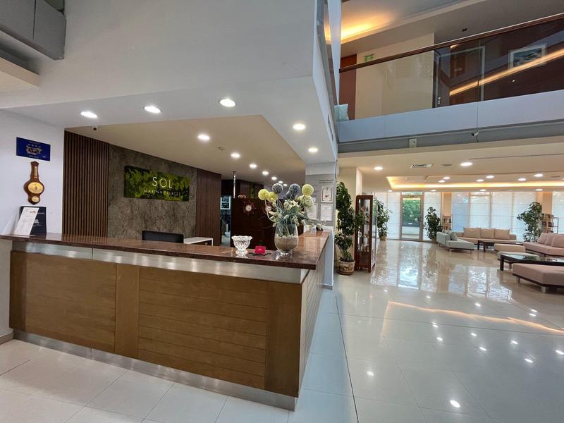 Moderner Empfangsbereich mit Holztheke, weißem Boden und Sitzecke in hellem, offenem Raum.