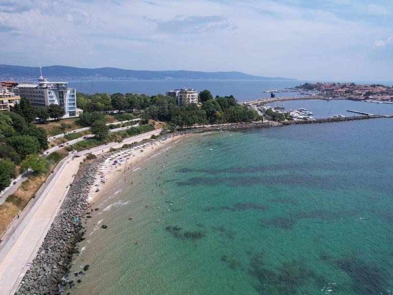 Küste mit Sandstrand, türkisfarbenem Wasser und umliegenden Gebäuden entlang der Straße.