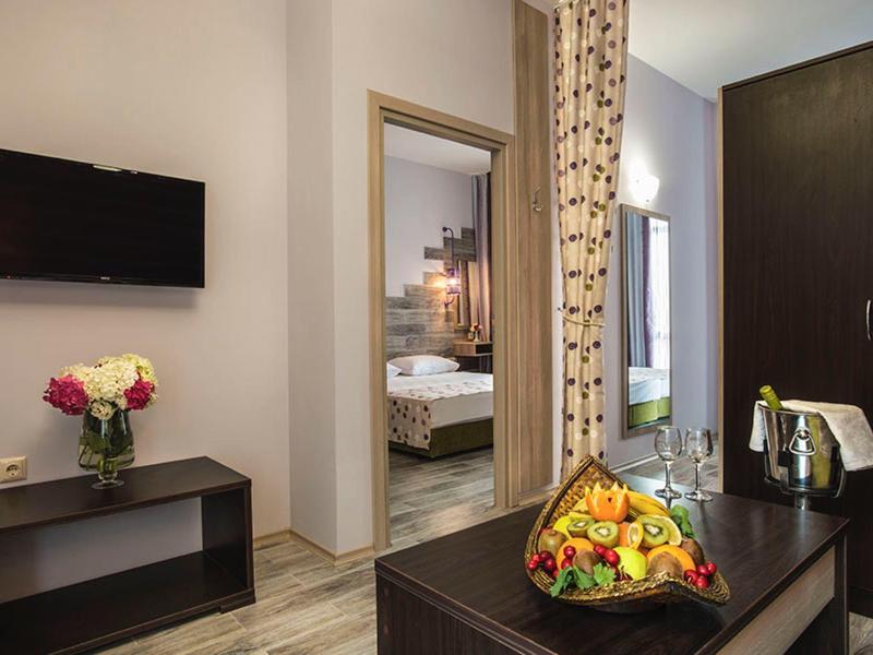 Modern eingerichtetes Hotelzimmer mit TV, Blumenstrauß und Blick ins Schlafzimmer.