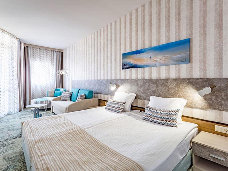 Modern eingerichtetes Hotelzimmer mit Doppelbett, Sitzecke und großem Fenster.