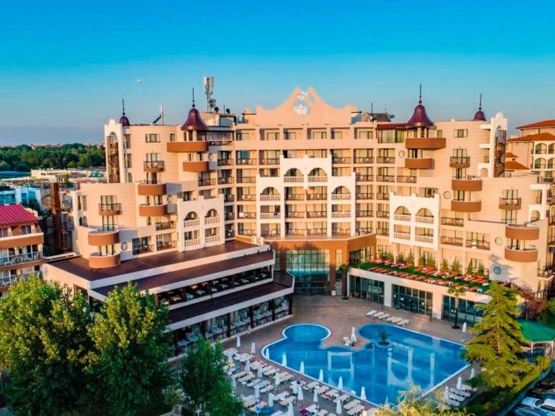 Großes Hotel mit Pool, umliegenden Liegestühlen und mediterraner Architektur bei blauem Himmel.