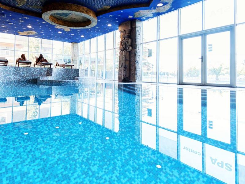 Hellblauer Indoor-Pool mit großen Glasfenstern und klarer Wasseroberfläche unter Sternenhimmel-Decke.