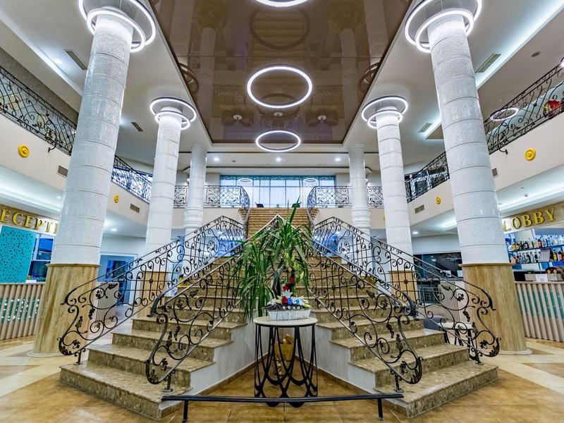 Große helle Bibliothek mit weißen Säulen, dreifacher Treppe und modernen Rundlichtern.