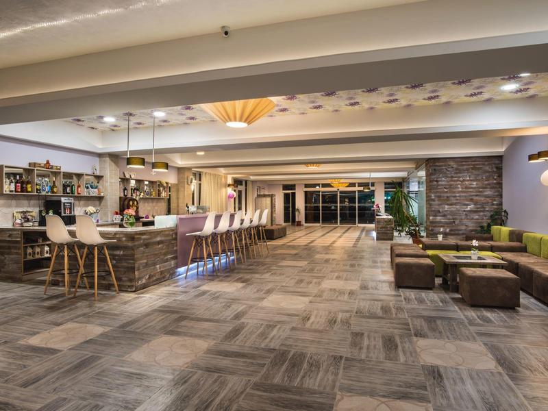 Großer Raum mit moderner Bar, weißen Stühlen, Sofas und industriellem Design, heller Beleuchtung.