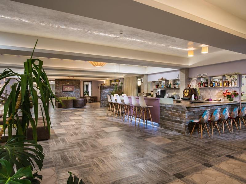 Großer, moderner Barbereich mit Holzfußboden, Theke, Barhockern und Pflanzen in hellem Ambiente.