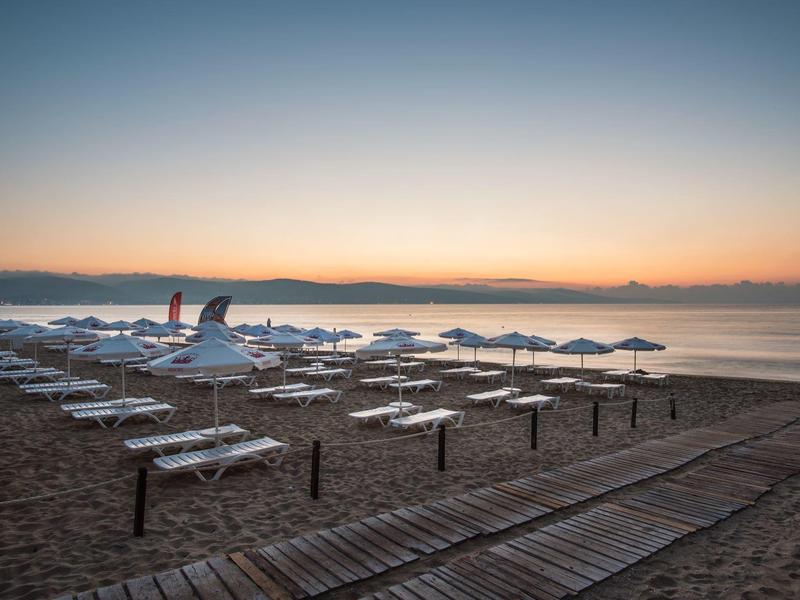 Strand mit Liegen und Schirmen, Holzsteg führt zum ruhigen Meer bei Sonnenuntergang.