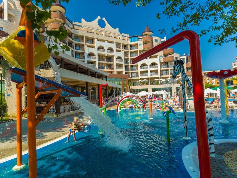 Wasserpark mit Rutschen, Planschbecken, bunten Wasserspielen und mehrstöckigem Hotel im Hintergrund.