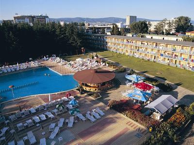 Großes Hotel mit Außenpool, Sonnenschirmen, Liegestühlen und umliegenden Gebäuden im Hintergrund.
