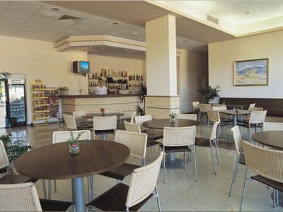 Area pranzo luminosa con tavoli, sedie, bar e vetrina con snack.