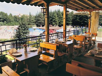 Terrazza coperta con tavoli e panche in legno con vista su piscina e bosco.