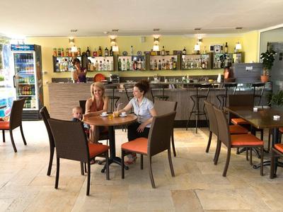 Gemütliches Café mit Holztischen, Stühlen und Bar, hell mit großer Fensterfront und Pflanzen.