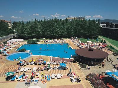 Großer Außenpool mit Sonnenschirmen, Liegestühlen, runder Bar und grünen Bäumen im Hintergrund.
