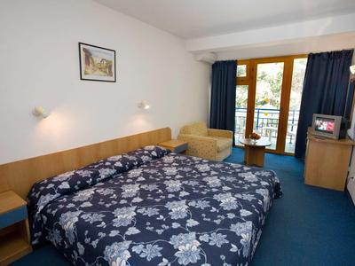 Gemütliches Hotelzimmer mit großem Bett, blauem Teppich und Balkon mit Holzgeländer.