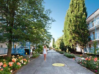 Pedone su un sentiero tra due edifici con alberi e fiori
