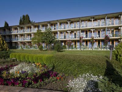 Edificio alberghiero a più piani con balconi e giardino ben curato davanti.