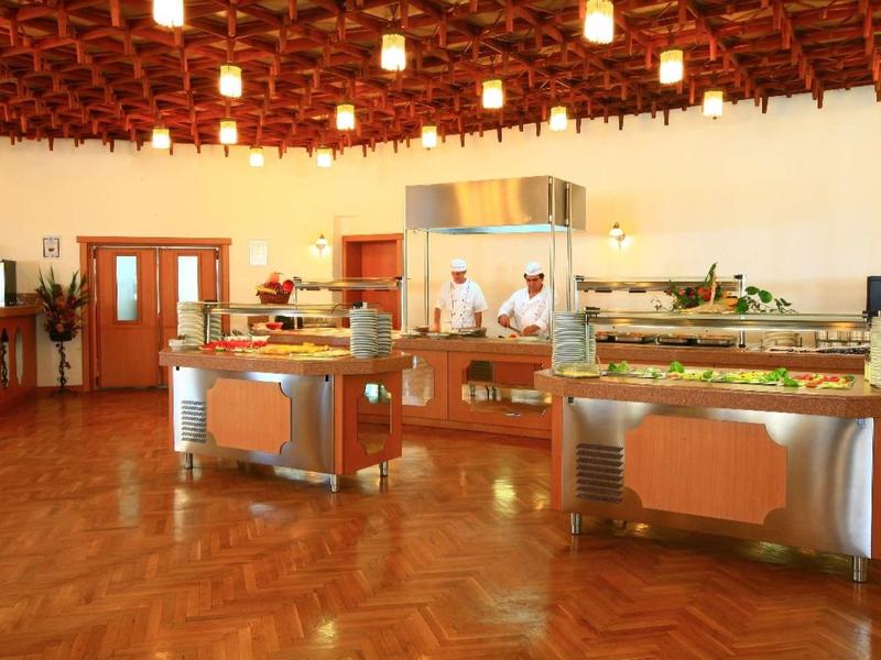 Großer Speisesaal mit warmem Holzfußboden, beleuchtet von vielen Deckenlampen und Buffet-Tischen.