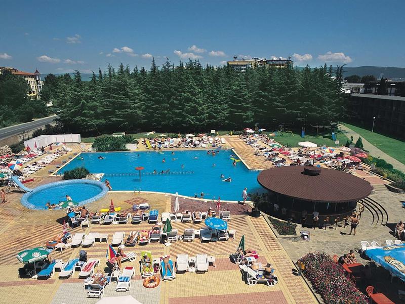 Großer Außenpool mit Sonnenschirmen, Liegestühlen, runder Bar und grünen Bäumen im Hintergrund.