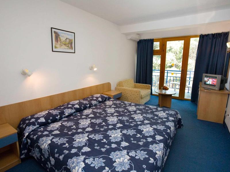 Gemütliches Hotelzimmer mit großem Bett, blauem Teppich und Balkon mit Holzgeländer.