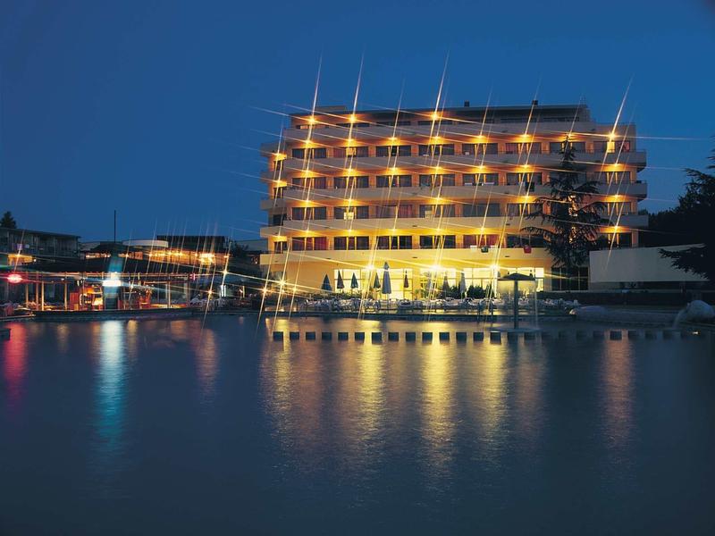 Beleuchtetes Hotel am Wasser mit Spiegelung der Lichter im ruhigen See bei Abenddämmerung.