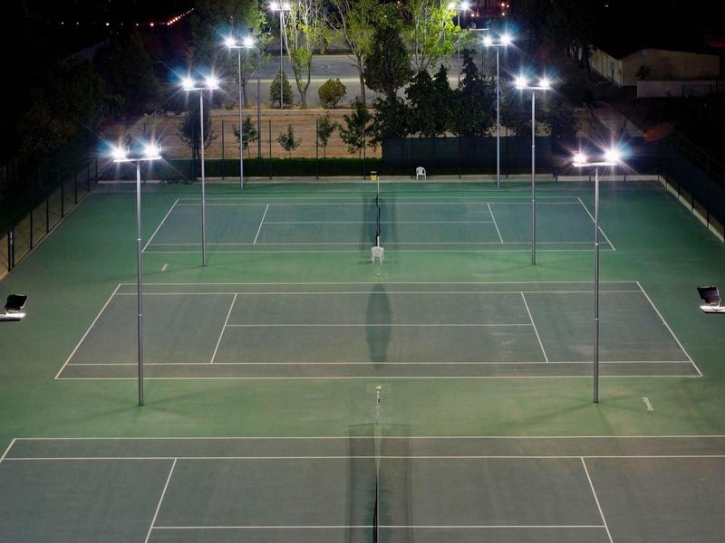 Strandterrasse mit Holztischen, Stühlen, einer weißen Pergola und Blick auf das blaue Meer.