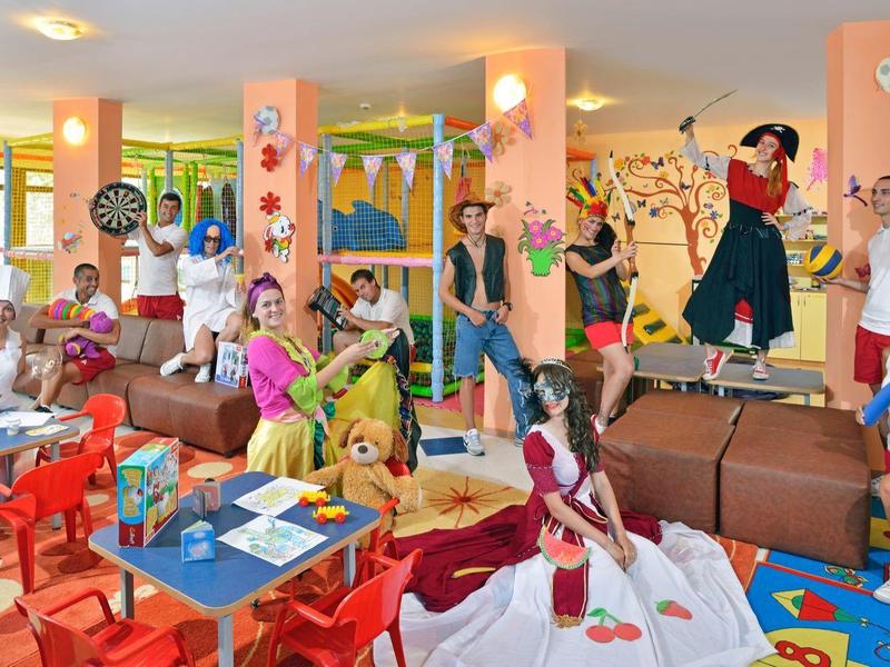 Bunte Kinderspielhalle mit Tischen, Stühlen und spielenden Kindern in lebendigem Umfeld.