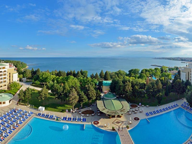 Großer Poolbereich mit Liegen, umgeben von Hotels und Blick auf den weitläufigen Strand und das Meer.