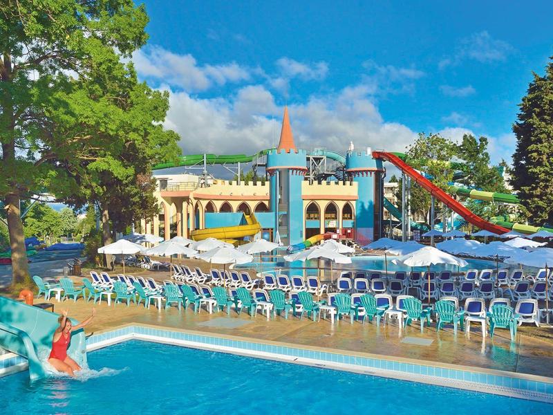 Außenpool mit Wasserrutsche, Sonnenschirmen und vielen Liegestühlen in einer Hotelanlage.