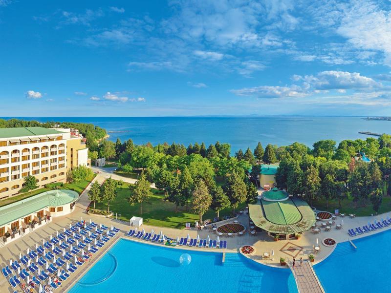 Hotel mit großem Pool und Sonnenliegen in grüner Umgebung am Meer.
