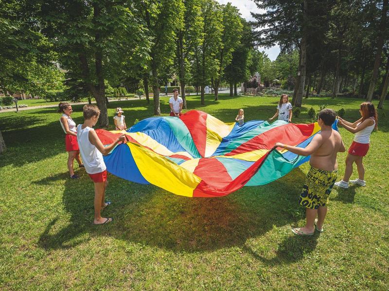 Kinder spielen mit einem bunten Fallschirm auf einer grünen Wiese im Park.
