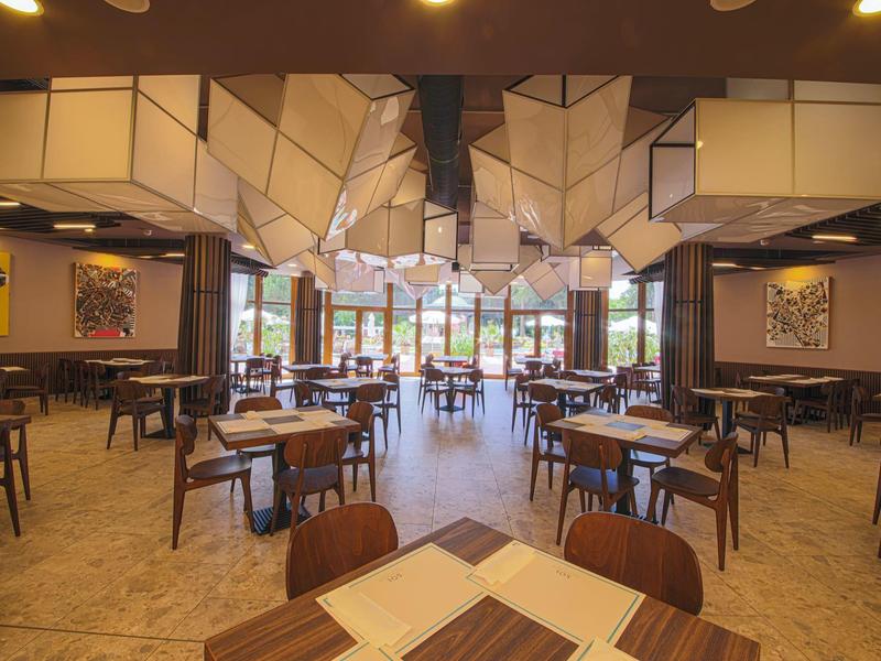 Modernes Restaurant mit geometrischen Deckenlampen und Holztischen in hellem Raum.