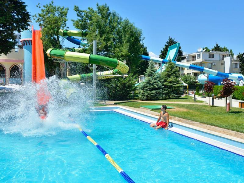 Erwachsener taucht im Pool herunter, Wasserrutschen und Bäume im Hintergrund.